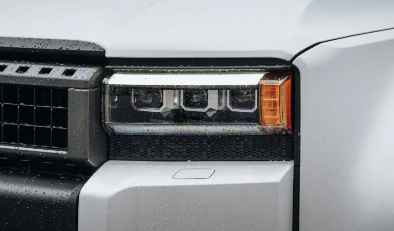 Close-up of new Toyota Land Cruiser front grille and LED headlights with orange accents, wet surface