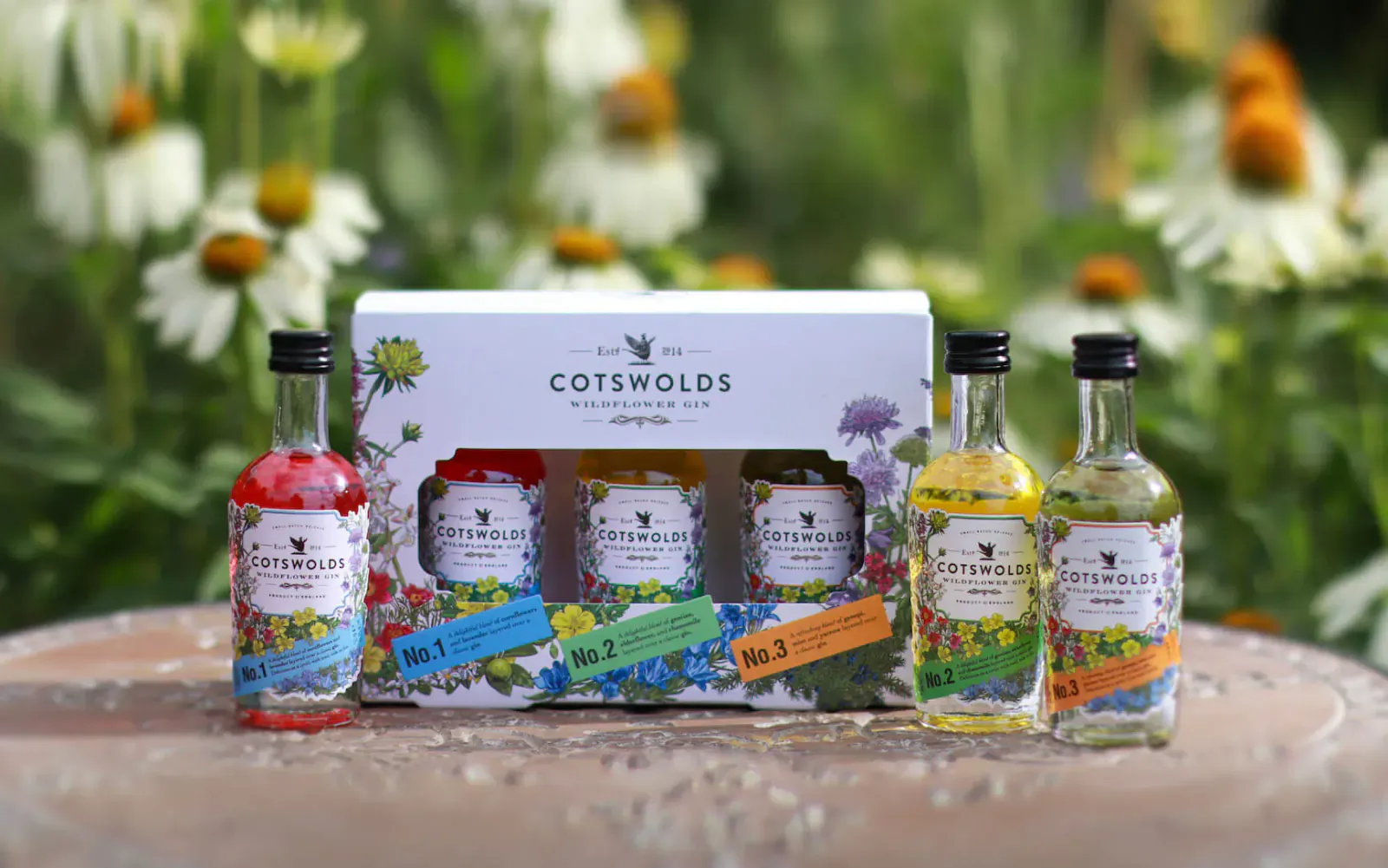 Cotswolds Wildflower Gin set in white box with 5 colorful mini bottles on wooden table amid daisies, for Mother's Day.