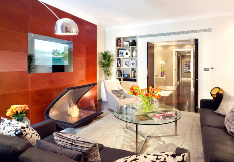 Modern luxury living room in Taj 51 Buckingham Gate with red wood wall, curved fireplace, orange tulips, glass coffee table, and leather sofa.