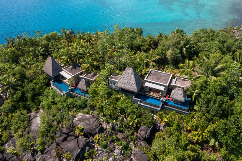 Aerial view of Anantara Seychelles luxury thatched villas with infinity pools on lush tropical cliffside over turquoise lagoon