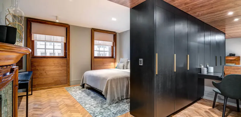 Elegant hotel bedroom at Apex Temple Court with king bed, black wardrobe, wooden desk, and window views.