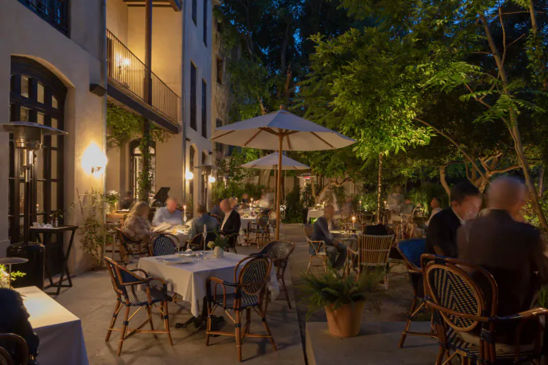 Evening outdoor dining at Can Bordoy Grand House & Garden, guests at candlelit tables under umbrellas amid lush trees and lit architecture.