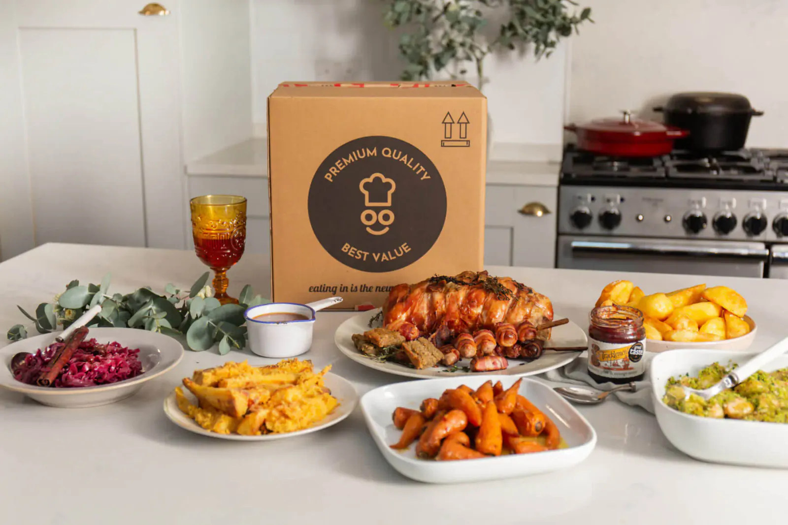 Premium 'Best Quality Best Value' chef box with Christmas dinner: roast pork, potatoes, carrots, beets, greens on kitchen counter.