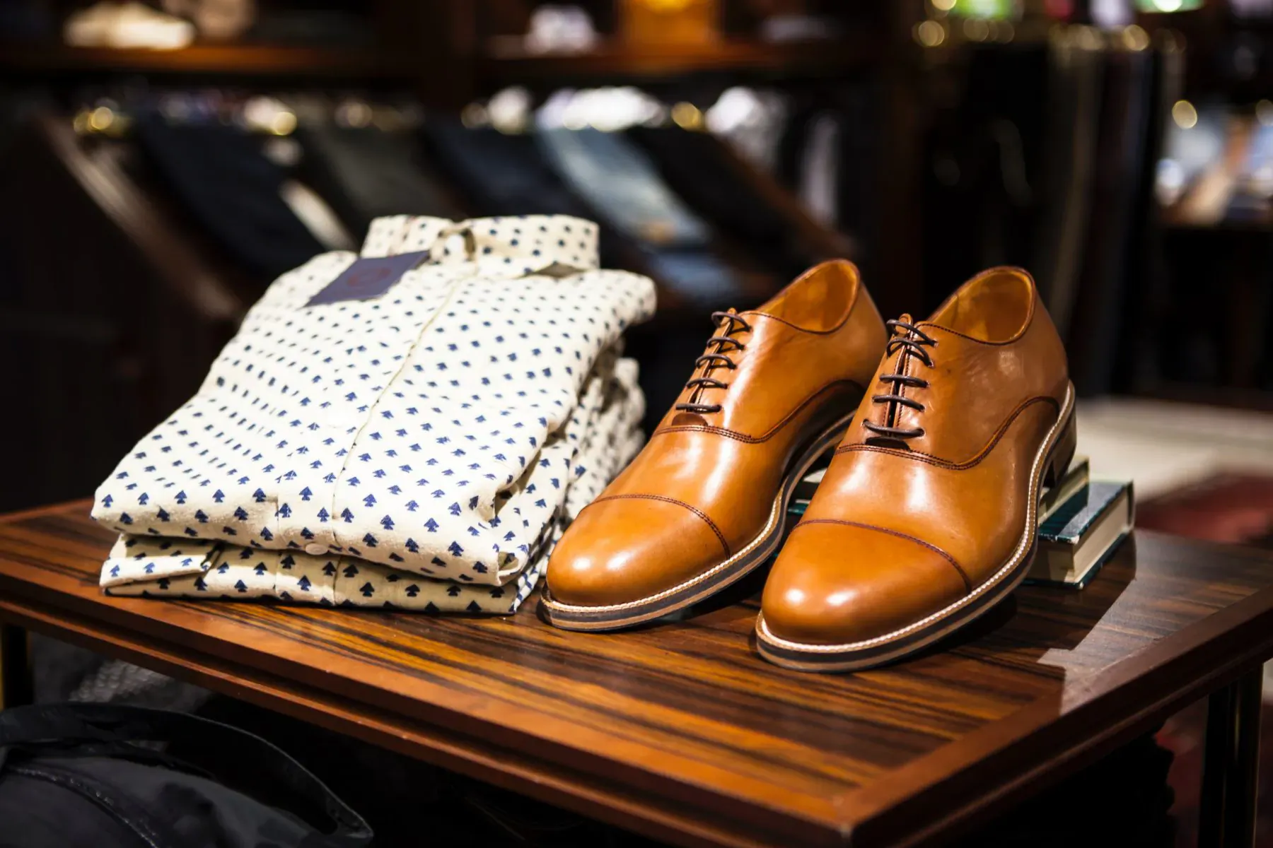 Folded white polka-dot shirts and tan leather dress shoes displayed on wooden table in upscale store