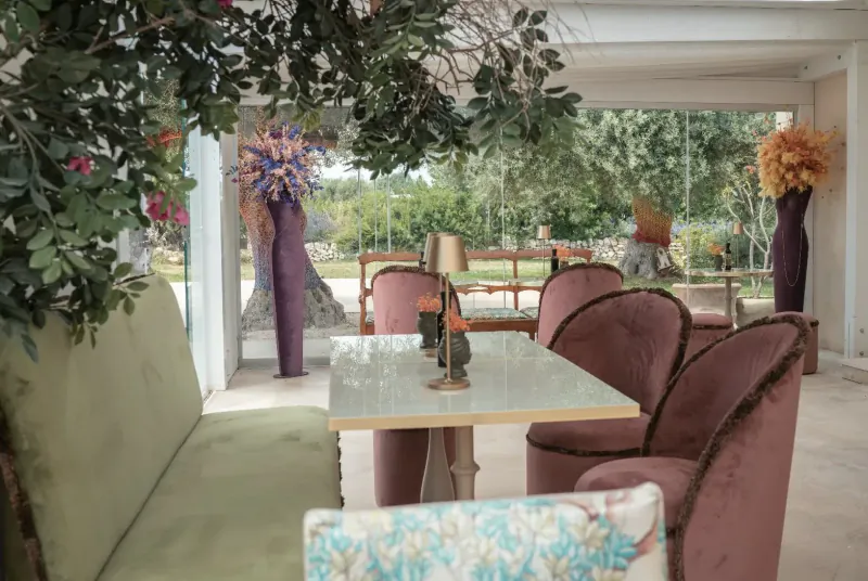 Elegant outdoor seating at Zahir Country House with green sofa, purple velvet chairs, glass table, and lush plants under pergola.