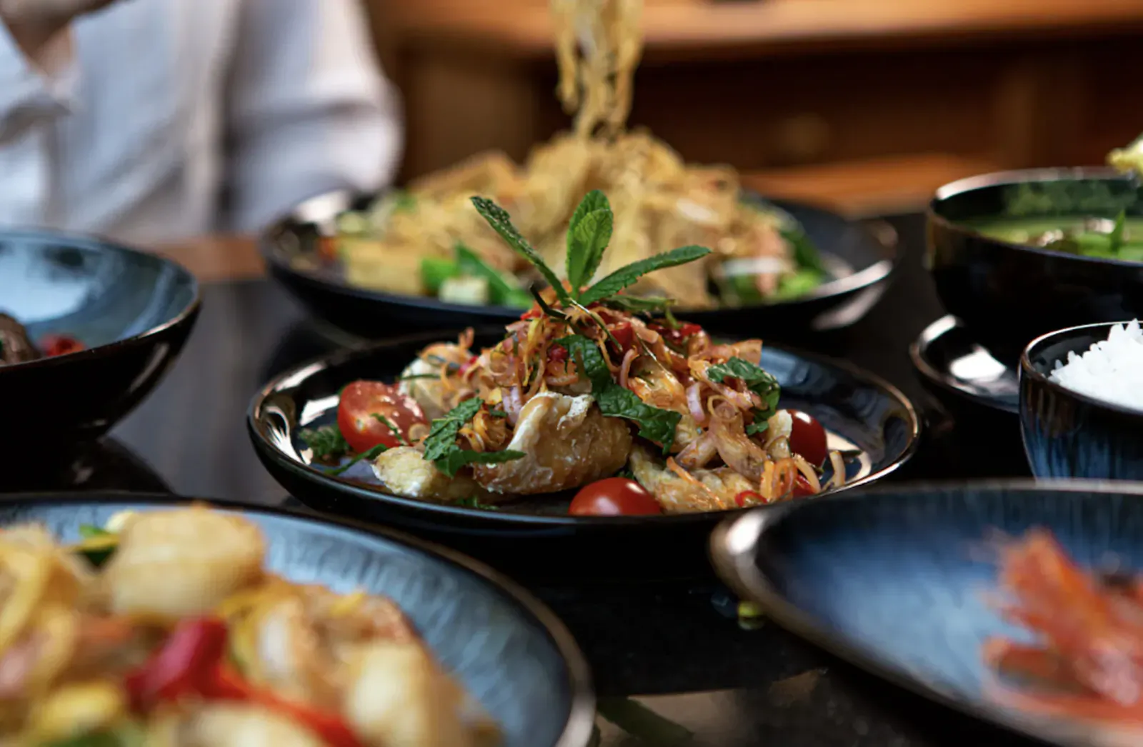 Assortment of authentic Thai dishes on black table: papaya salad, noodles, rice, and seafood, at Nipa Thai London