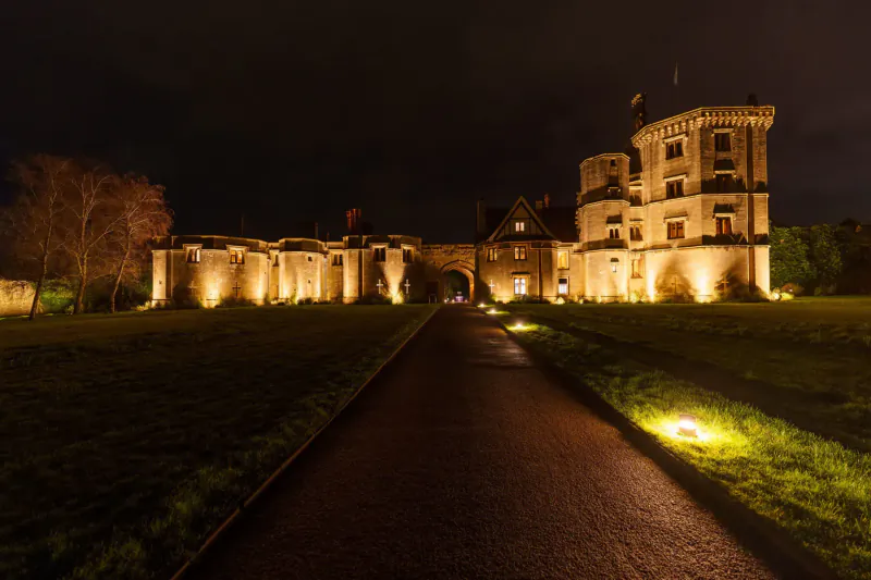 Thornbury Castle hotel in Bristol at night, illuminated with lights along driveway and towers glowing.