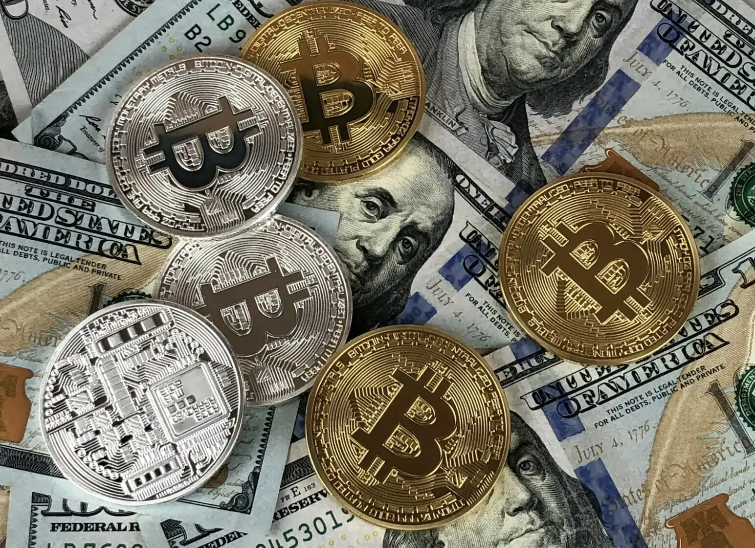 Close-up of scattered US dollar bills with gold and silver Bitcoin coins.