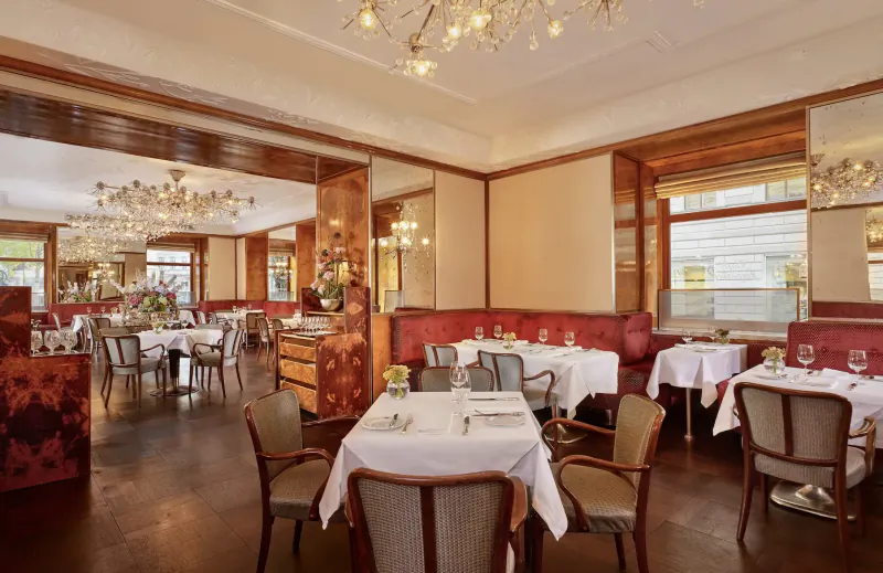 Elegant dining room in Hotel Imperial Vienna with wooden paneling, chandeliers, white tablecloths, and red banquettes.