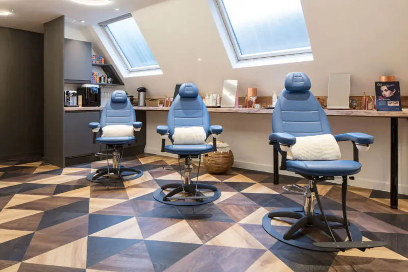 Three blue adjustable salon chairs with white neck pillows at a counter in modern Medispa with skylights and wood floor.