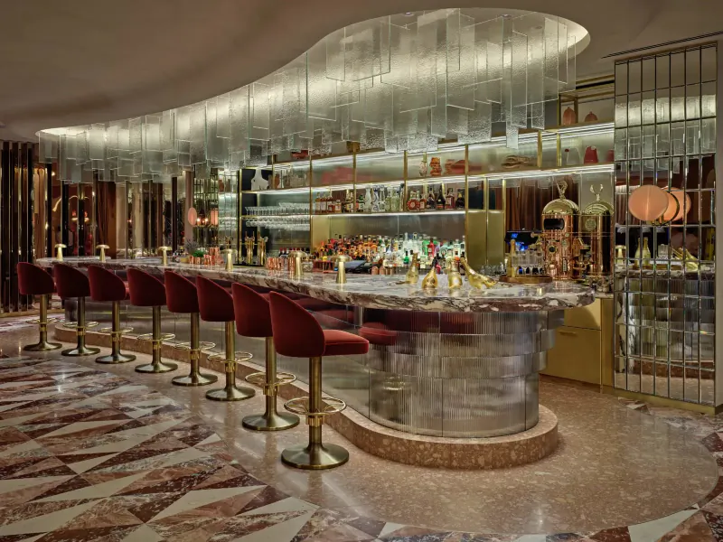 Park Corner Brasserie bar at London Hilton on Park Lane: curved counter with red stools, lit shelves of bottles, terrazzo floor.