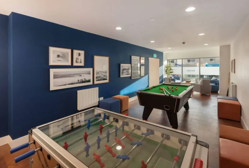 Modern recreation room with green pool table, foosball table, seating, and ocean photos on navy walls.