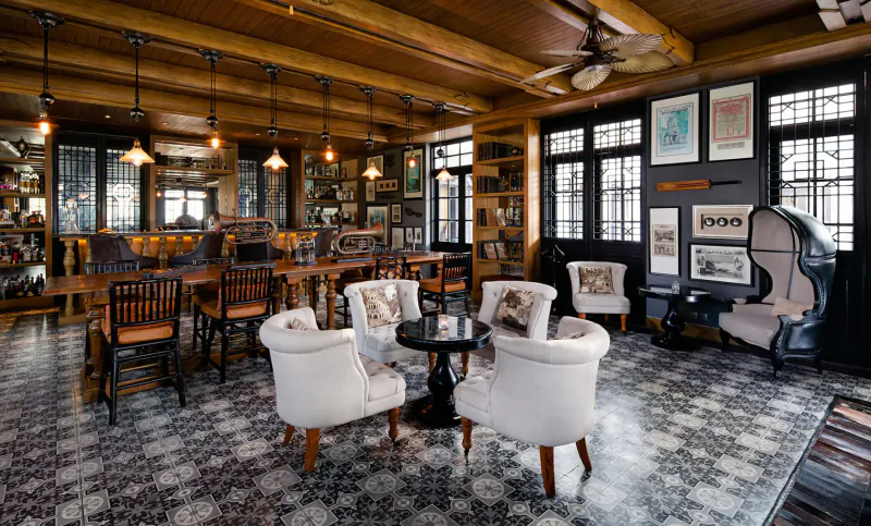 Elegant wooden-beamed lounge at The Sanchaya with white armchairs, bar, art, and checkered tile floor