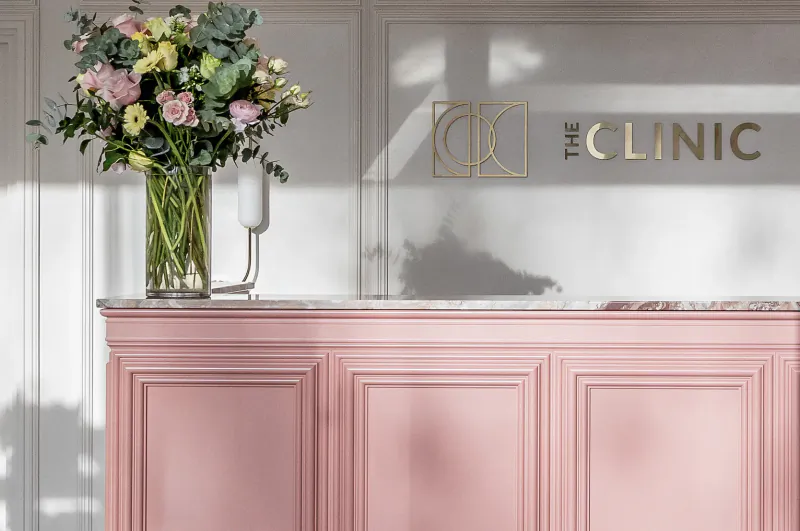 Pink reception desk at The Clinic with colorful flower bouquet and gold logo on white wall