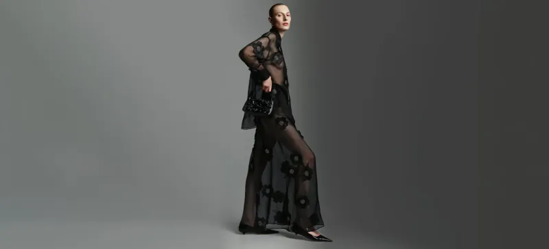 Model poses sideways in sheer black lace Scanlan Theodore gown on gray background