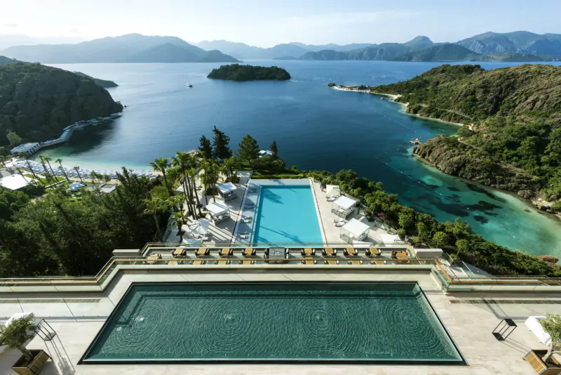 Aerial view of infinity pool at luxury resort overlooking turquoise bays and lush green mountains.