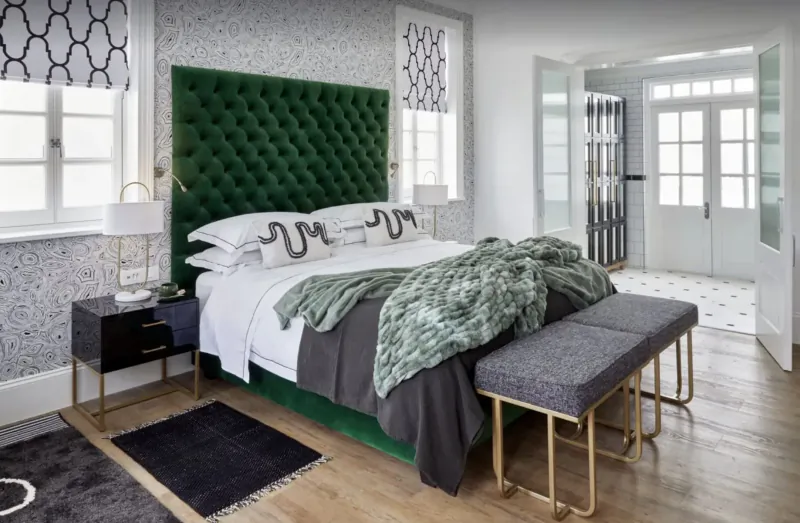 Luxurious bedroom at Cape Cadogan Boutique Hotel with green velvet tufted headboard, white bedding, green throw, bedside tables, and open doors to balcony.