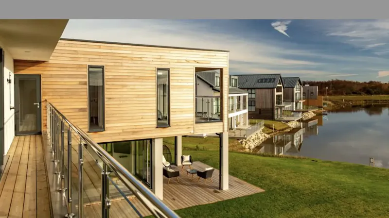 Modern cedar-clad luxury homes on elevated wooden deck overlooking lake and green fields at Silverlake Dorset
