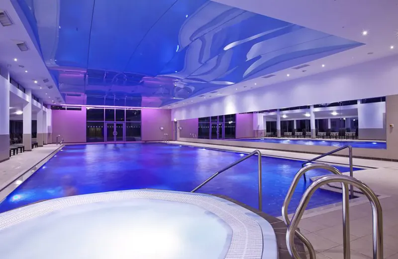 St. Brelade’s Bay Hotel indoor pool with glowing blue water, spa, mirrors, and lounge chairs.