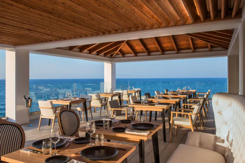 Elegant outdoor restaurant at Abaton Island Resort with wooden-beamed ceiling, set tables, and sea view.