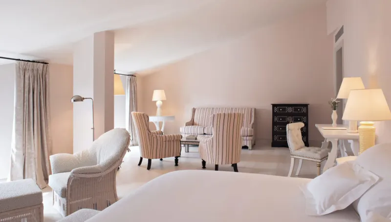 Elegant Hotel Cappuccino suite with pink walls, white upholstered armchairs, sofa, bed, and lamps.