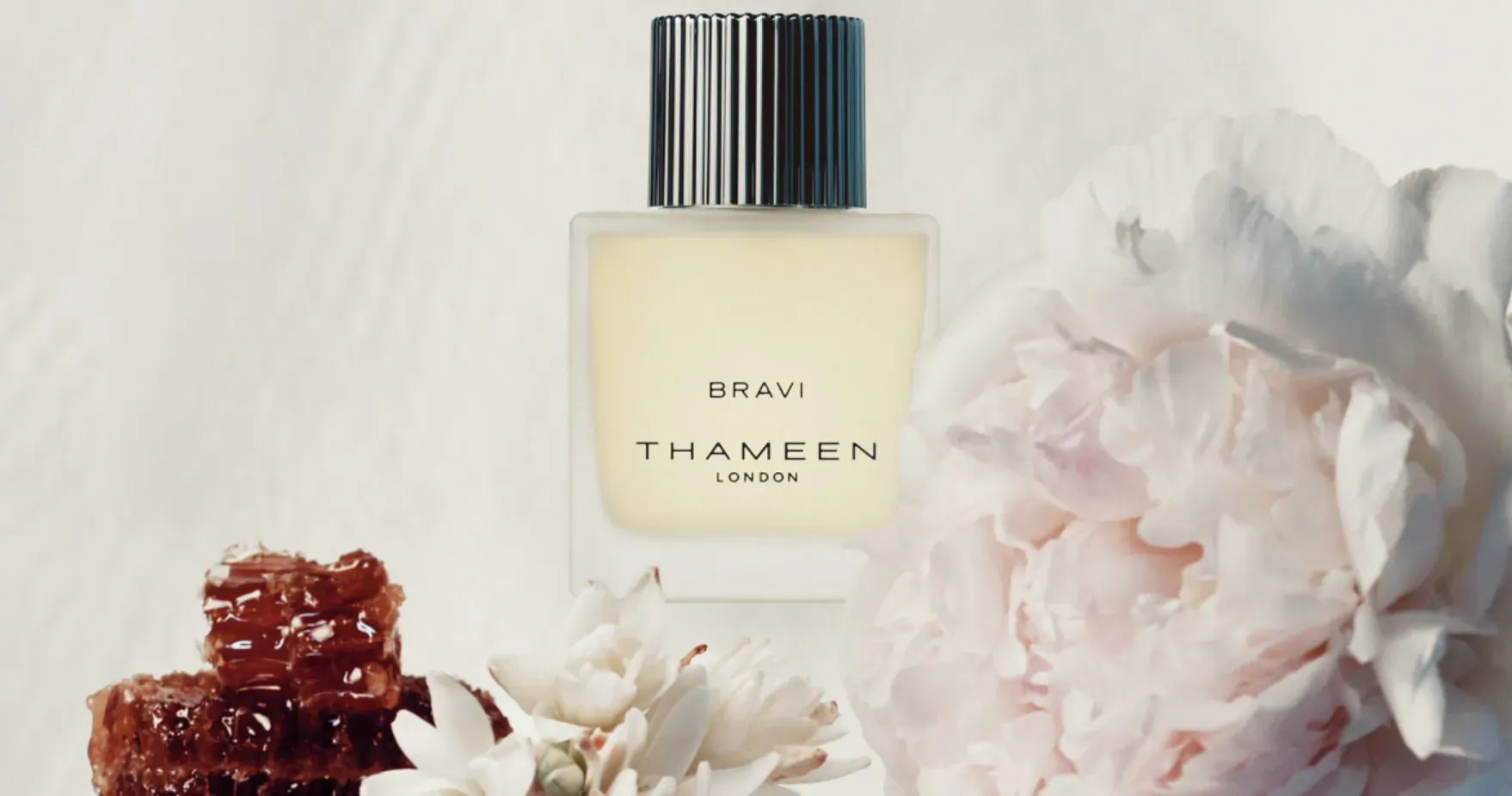 Thameen Bravi perfume bottle on white background with white peonies and honeycomb. Text: BRAVI, THAMEEN LONDON.