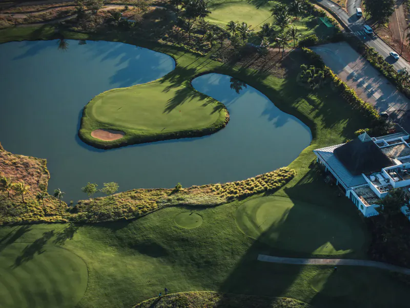 Aerial view of Mauritius golf course with heart-shaped island green in pond, fairways, clubhouse, and trees.