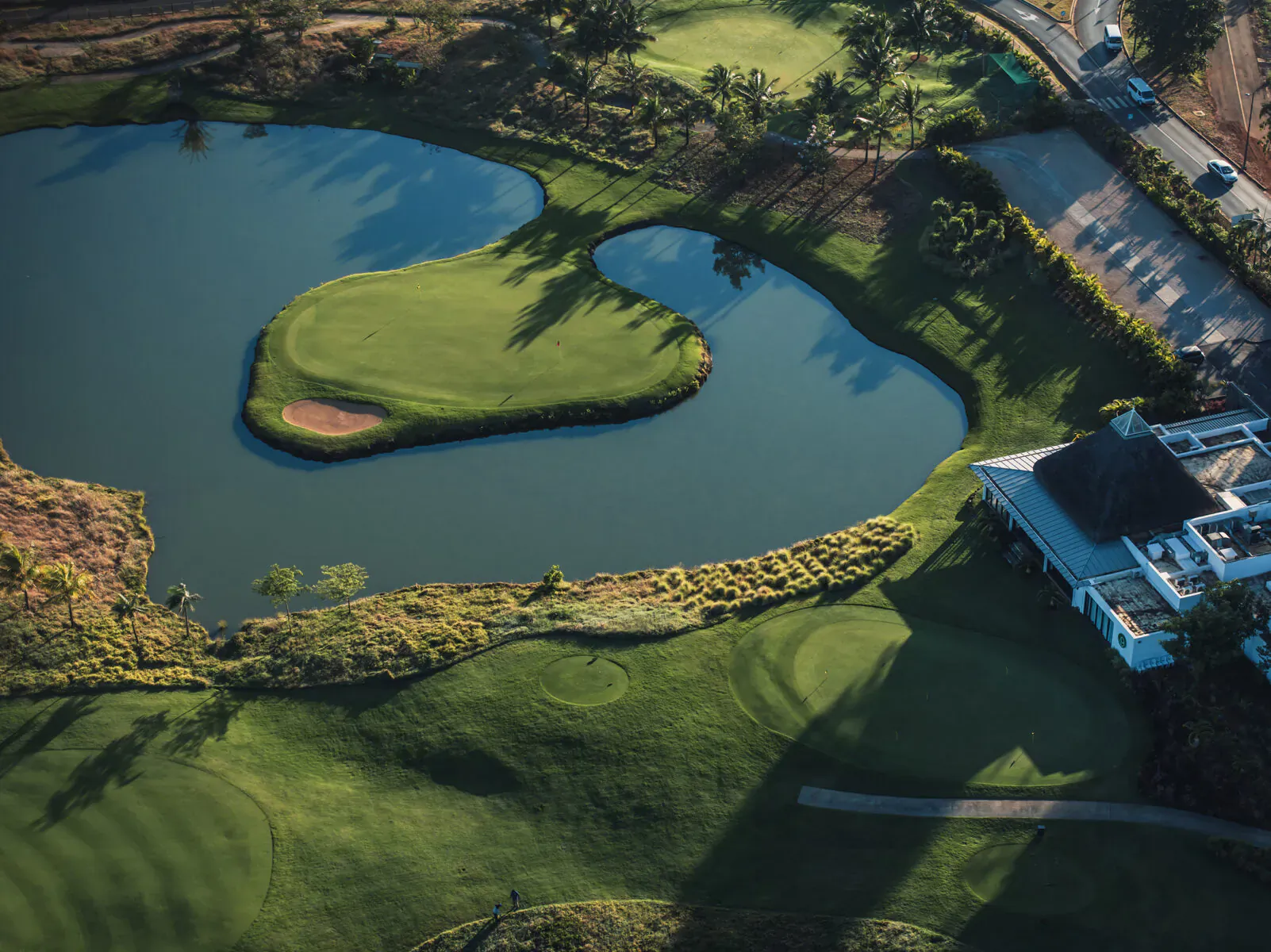 Aerial view of Mauritius golf course with heart-shaped island green in pond, fairways, clubhouse, and trees.