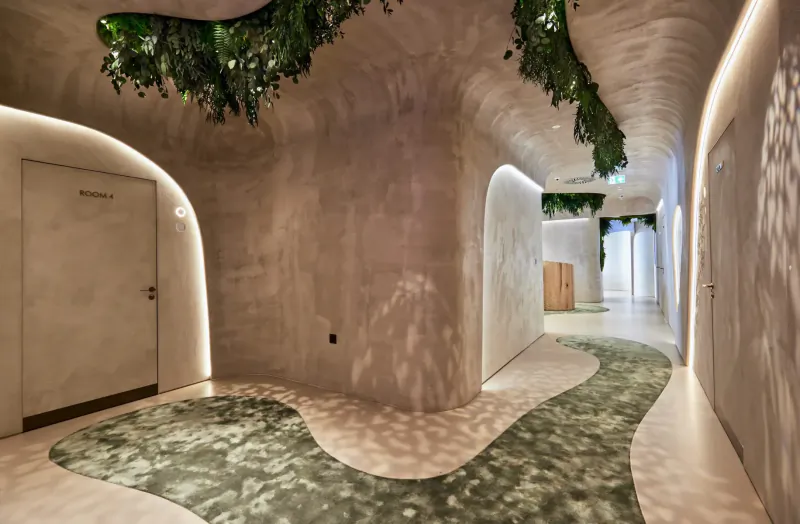 Curved corridor in HVN Knightsbridge wellness centre with hanging greenery, wave-patterned floor, and soft lighting.