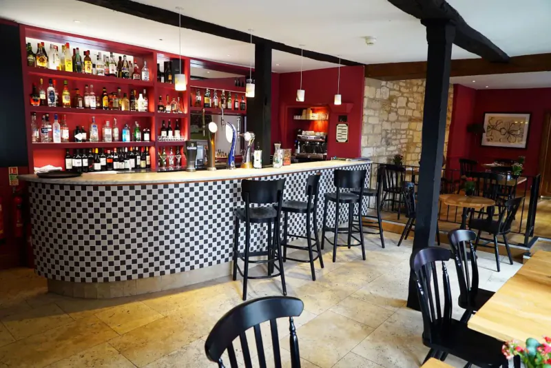 Elegant hotel bar with curved black-and-white tiled counter, wooden stools, extensive liquor shelves, and bistro tables.