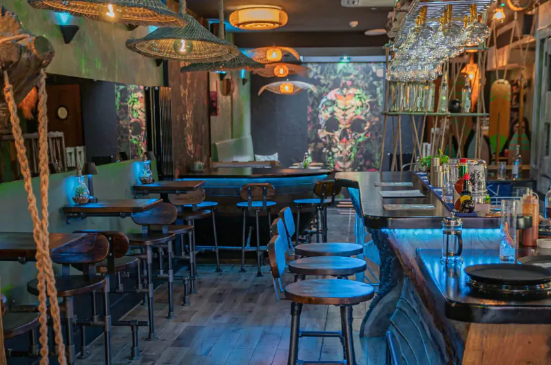 Mezcalito Mexican bar in Islington: rustic interior with wooden bar stools, glowing lamps, neon accents, and liquor shelves.