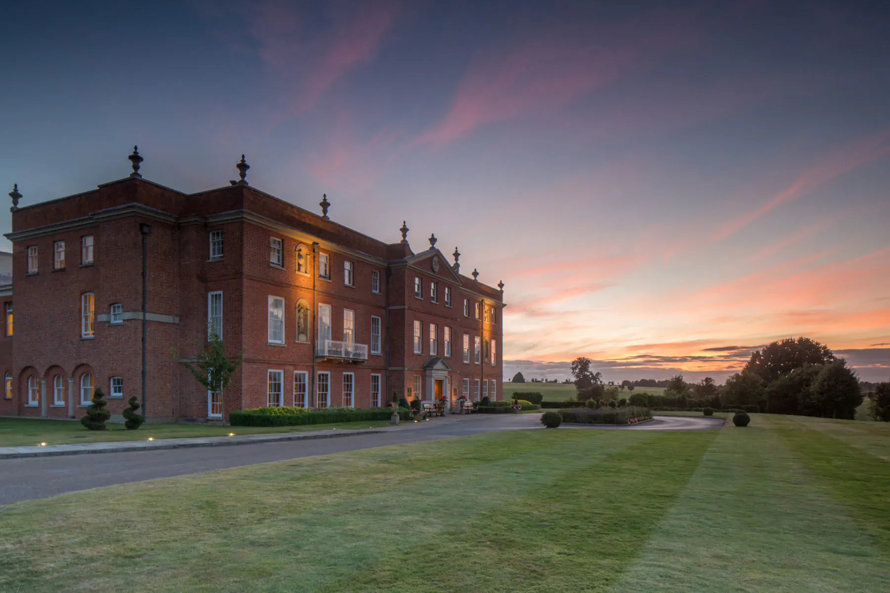 Four Seasons Hampshire, grand red brick manor house at sunset with manicured lawns and pink sky.