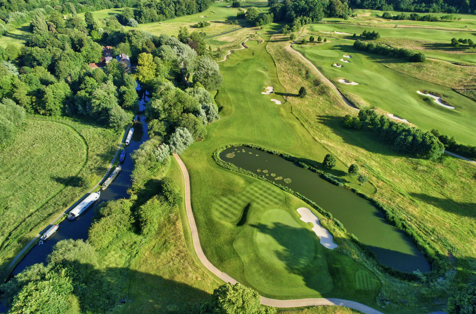 Aerial view of lush green golf course at The Grove with tree-lined fairways, ponds, and paths