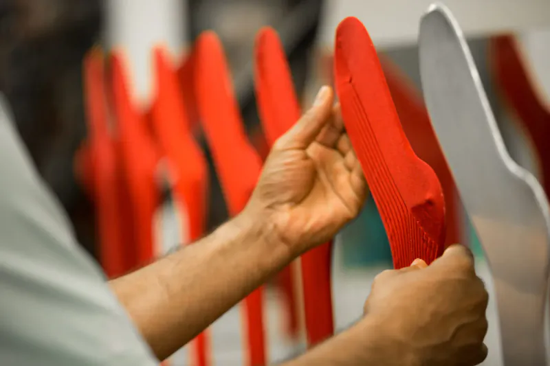 Worker holding red chair among row of red chairs and white one in factory gallery