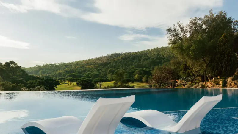 White lounge chairs by infinity pool overlooking green hills and blue sky at Penha Longa Resort.