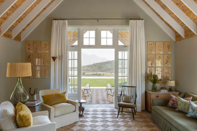 Elegant Franschhoek living room with white beamed ceiling, plush seating, open French doors to garden and mountains.