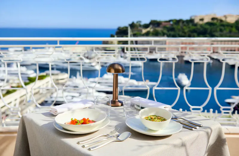 Elegant outdoor table with two bowls of soup at Michelin restaurant in Monaco, marina and sea view.