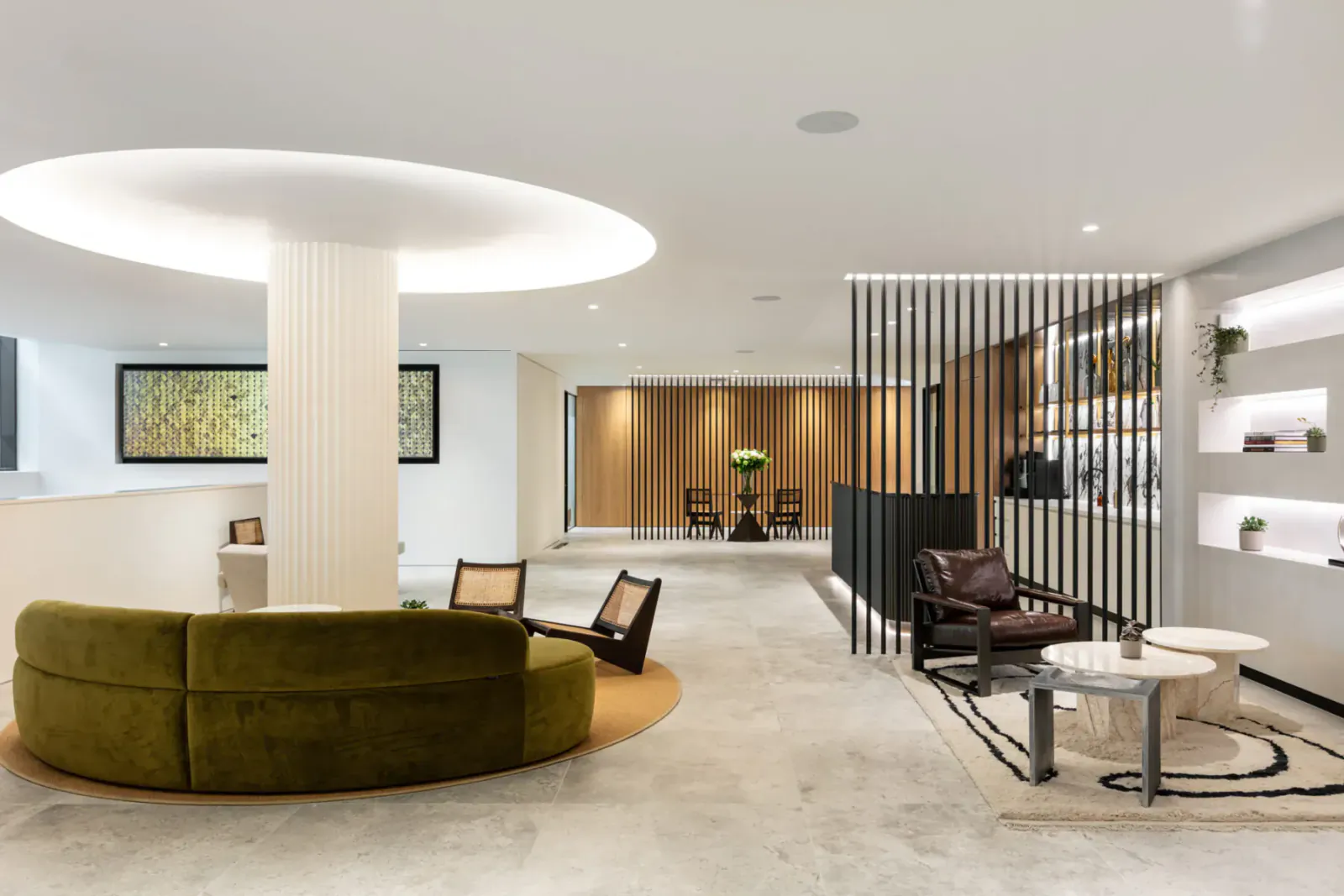Modern hotel lobby with curved green velvet sofa, rattan chairs, wooden screen dividers, plants, and art.