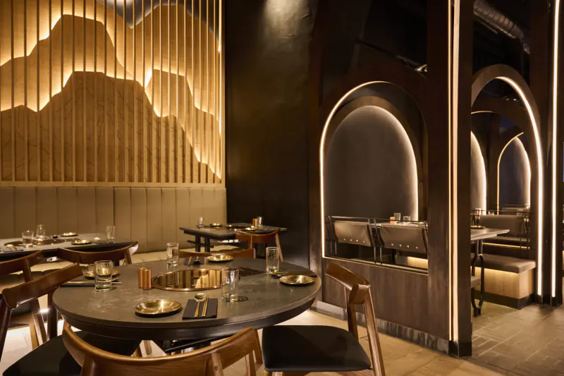 Modern Korean restaurant interior with wooden mountain wall art, arched booths, round table set with plates and glasses.