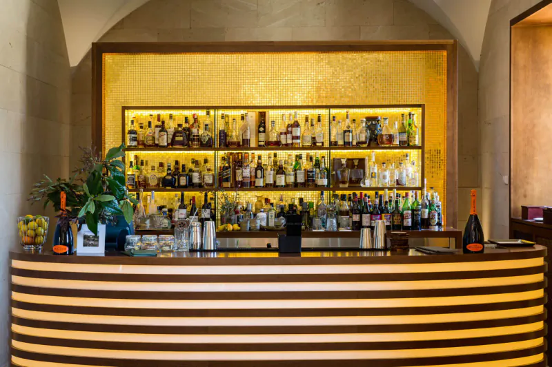 Elegant curved wooden bar with extensive backlit liquor shelves and plants at Castell Son Claret, Mallorca