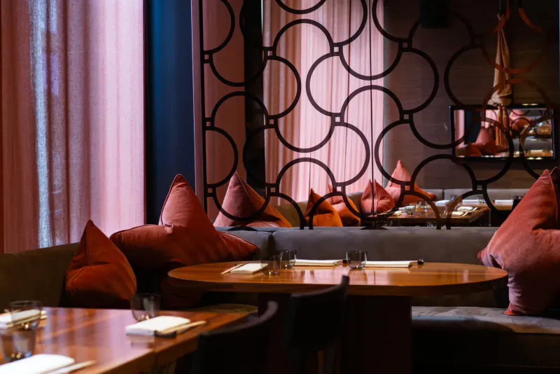 Elegant UMU Mayfair dining area with pink pillows on gray booth seating, round tables set with dishes, and patterned backdrop.