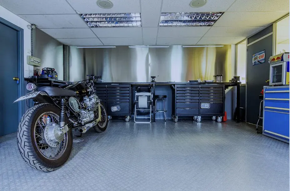 Black motorcycle parked in modern garage with blue tool cabinets, stainless steel walls, and storage hacks.