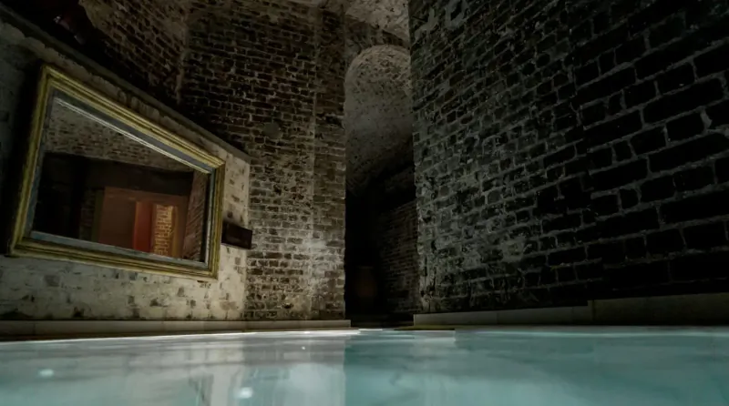 Tranquil ancient brick bathhouse with arched walls, ornate mirror reflecting red door, and glowing turquoise pool at Aire Ancient Baths.