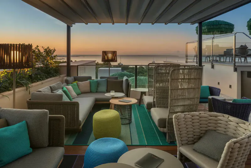 Rooftop lounge at El Llorenç Parc de la Mar with wicker furniture, cushions, sunset sea view.