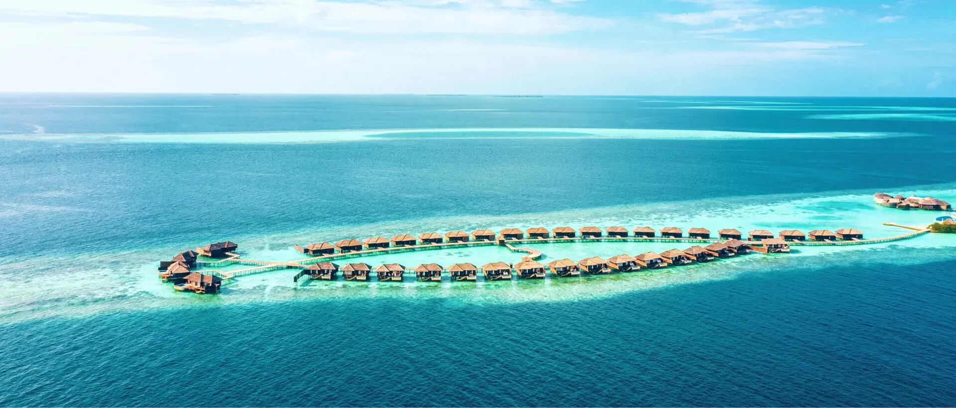Aerial view of Lily Beach Resort & Spa Maldives: curved overwater bungalows on turquoise lagoon