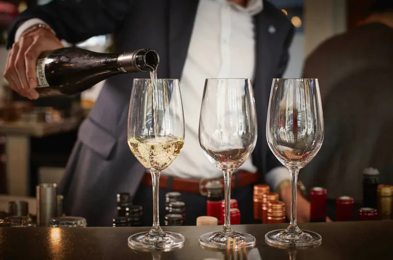 Man in suit pouring champagne from bottle into three wine glasses on bar counter at 28-50 Oxford Circus