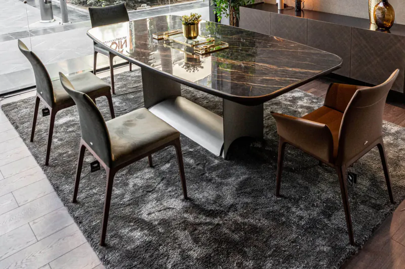 Modern oval marble dining table with six upholstered chairs on gray rug in stylish showroom