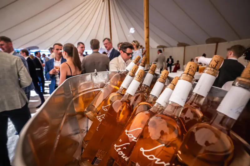 Close-up of Château Léoube rosé wine bottles in ice bucket at elegant Goffs London Sale event under tent with guests