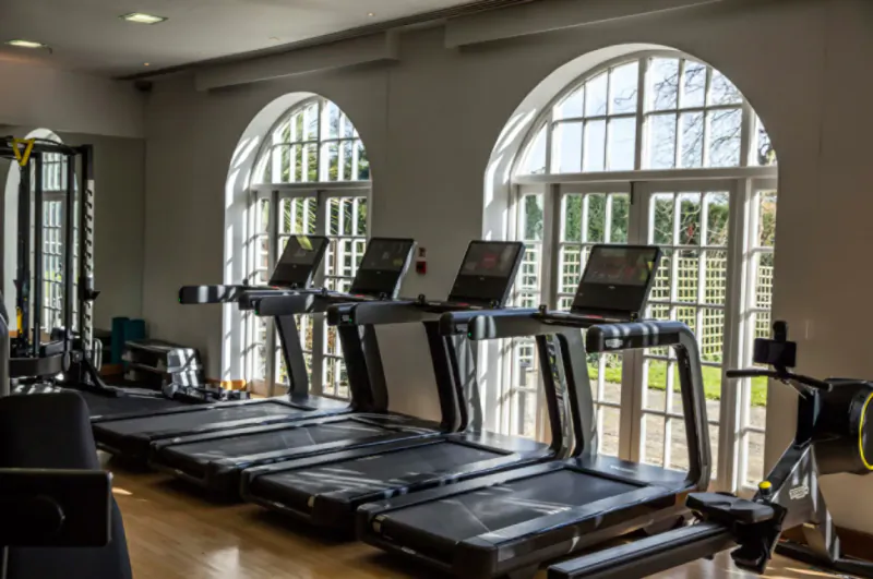 Row of modern treadmills in a luxurious gym with arched windows overlooking gardens at Four Seasons Hampshire.
