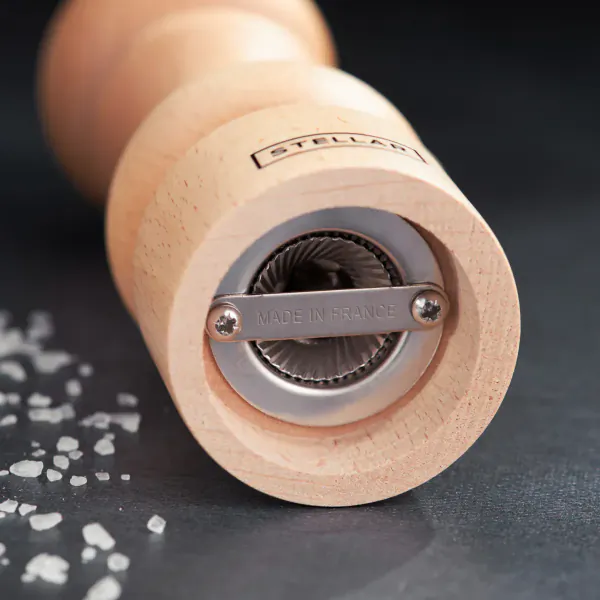 Close-up of Stellar wooden salt mill with 'Stellar' branding, metal grinder, and scattered salt grains
